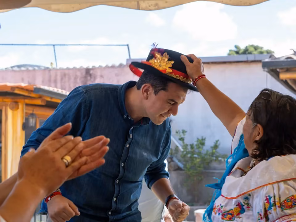 Harold Burbano mientras una mujer le coloca un sombrero durante un encuentro